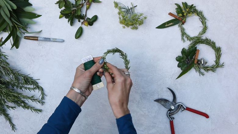 Person making miniature rosemary wreaths with a single stem of rosemary