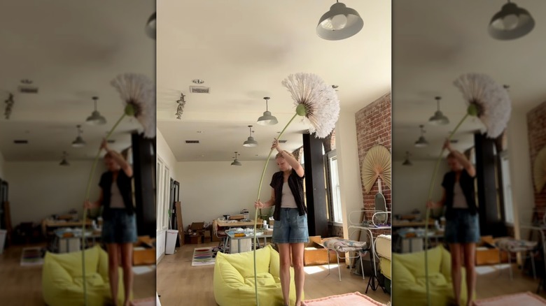 A large handmade faux dandelion towers over the person holding it upright in their living room.