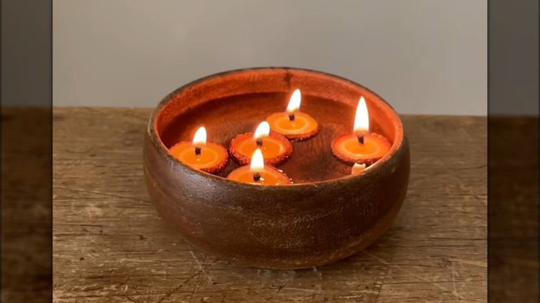 Lit acorn cap candles floating in a wooden bowl filled with water