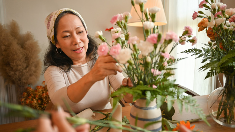 A person arranging pink and white flowers in a beige ceramic vase.