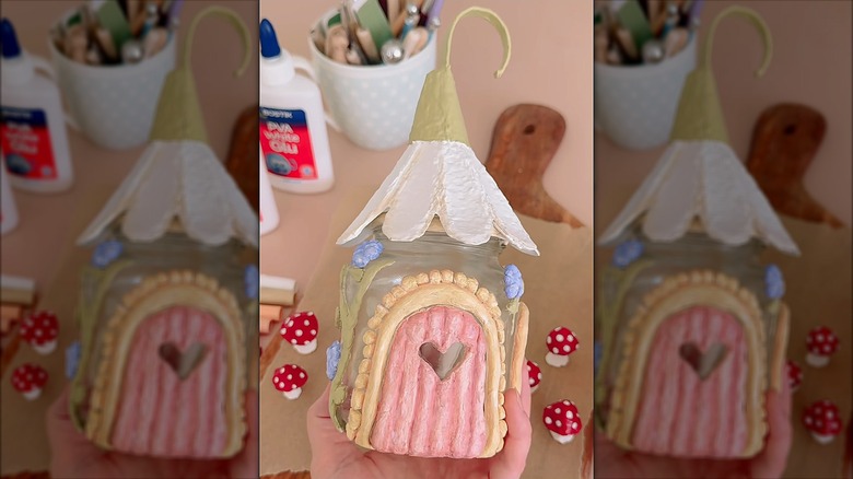 Glass jar decorated to resemble a miniature fairy house using colorful clay and a flower roof made of egg cartoon pieces