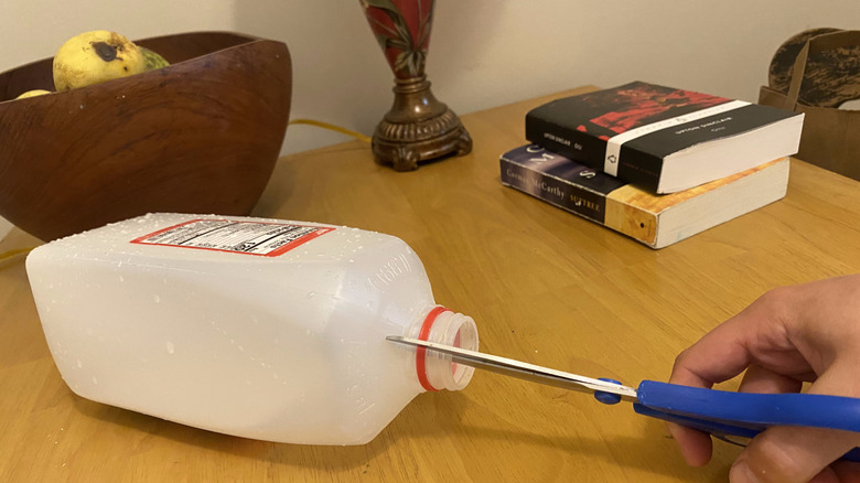 A hand holding scissors to cut open a plastic carton
