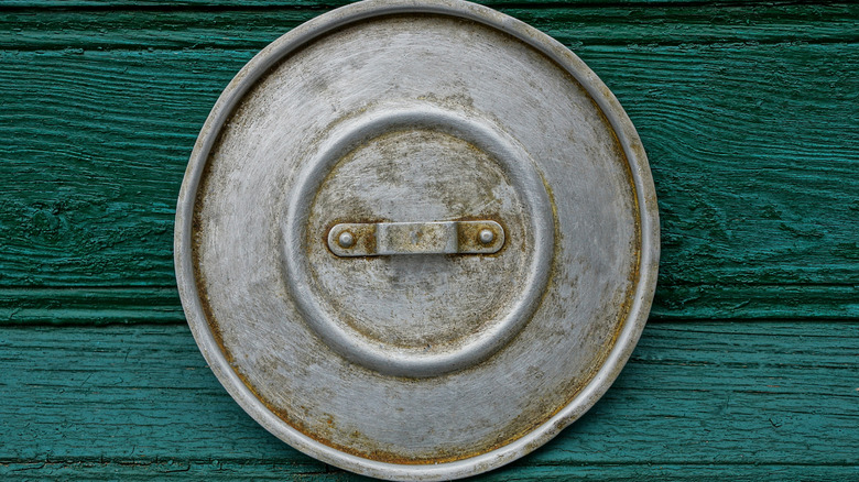 An old aluminum gray lid on a green wall.