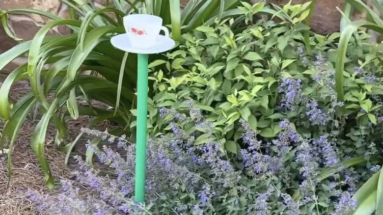 A white teacup and saucer set atop a green post in a garden