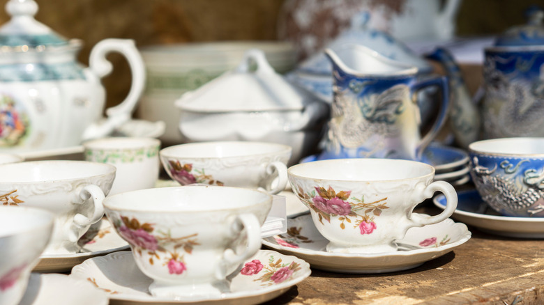 A variety of teacups and saucers arranged on a wooden table outdoors