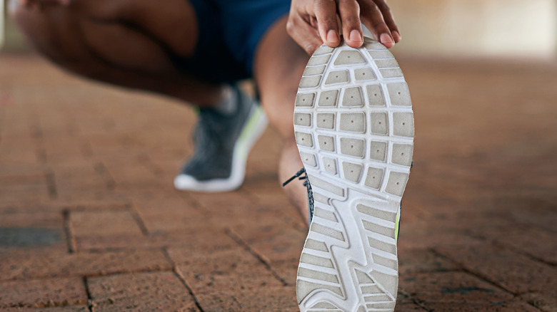 Fingertips holding the sole of a trainer up with a blurred body behind it. The sole is slightly grubby.