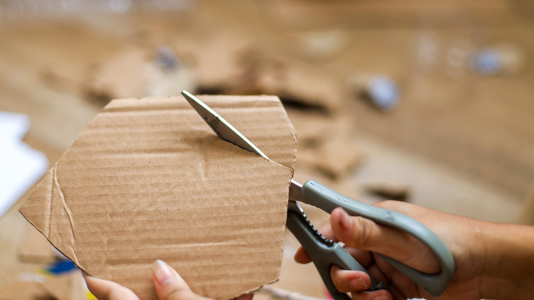 Hands cutting up cardboard with scissors.