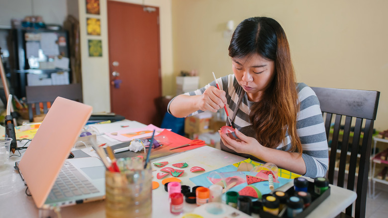 Woman sitting at table painting paper for a craft