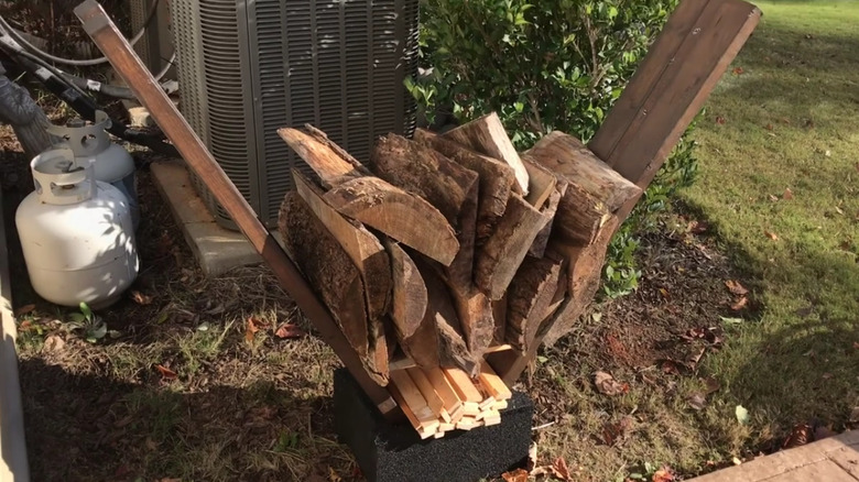 An outdoor firewood rack made from a cinder block and four planks of wood.