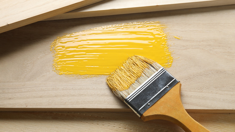A paintbrush with yellow paint sits on top of some wooden planks.