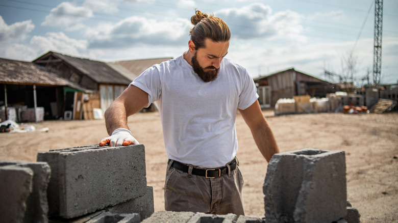 A man puts a gloved hand on a stack of cinder blocks at a landscape materials yard.