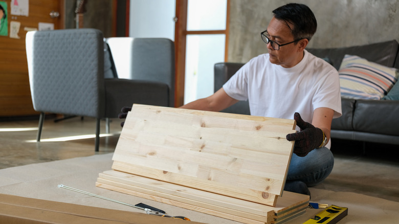 Man sitting on floor with stack of wood boards