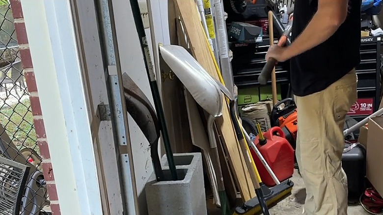 A person putting long-handled garden tools into the concrete block storage unit
