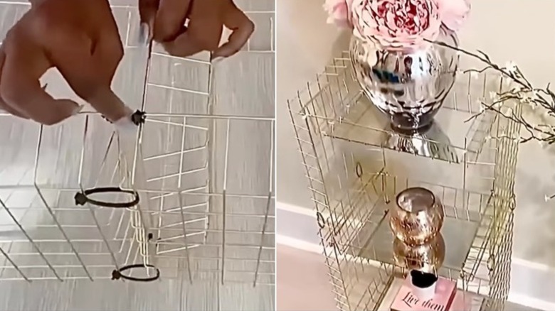 An accent table made of gold wire with mirrored shelves, holding a vase of flowers, a candle, and books.