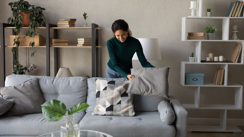 A woman placing a pillow on a couch.
