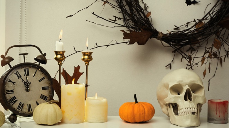 A white space and a white surface with Halloween decorations including a pumpkin, a skull, a bloody candle, a clock, and a dark wreath