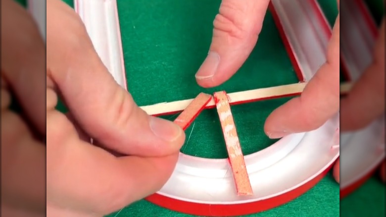 Two hands glue wooden pieces to a plastic frame.