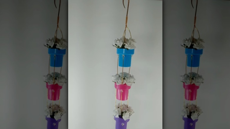 Three fabric softener caps hanging from wire with white artificial flowers inside them.
