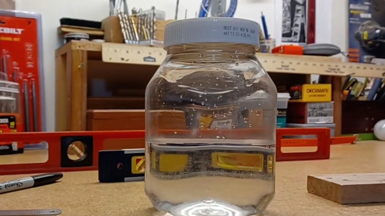 A DIY level made from a glass jar filled with water sits on a workbench next to a real level, a Sharpie, and a wooden block.
