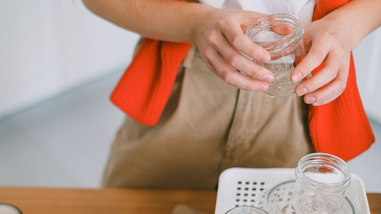 A person holds a glass jar in her hands above a white plastic basket full of more glass jars.
