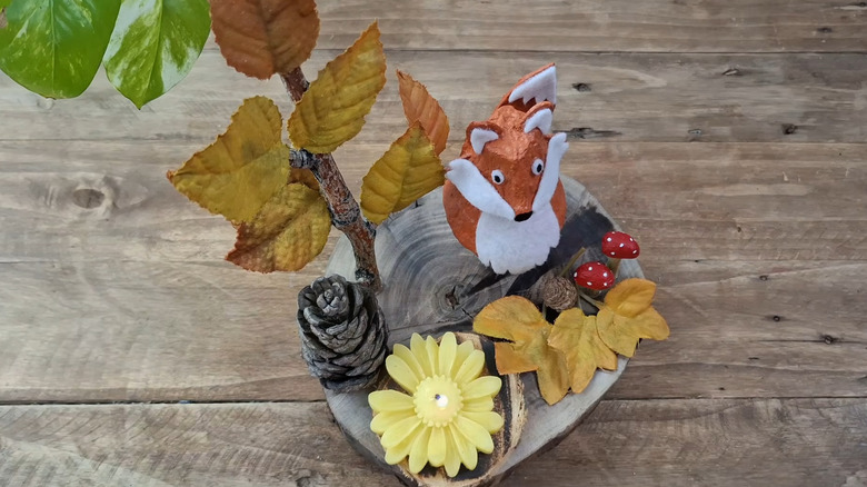 A log slice with a cute, painted fox, a branch of autumn leaves, pinecones and toadstools