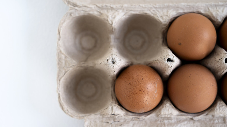 Close up of partially empty cardboard egg carton with brown eggs