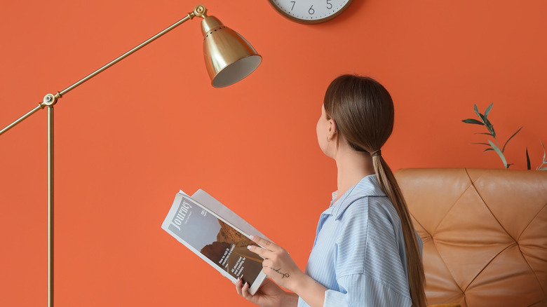 Woman in chair holding magazine with a gold floor lamp next to her