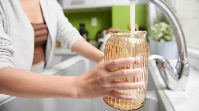 Woman rinsing a glass vase under running water