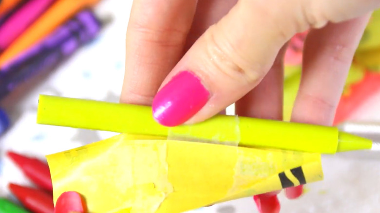 A woman peeling the paper wrapper from a yellow crayon.