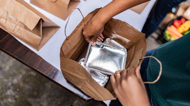 A person opening a bag to reveal metal takeout containers
