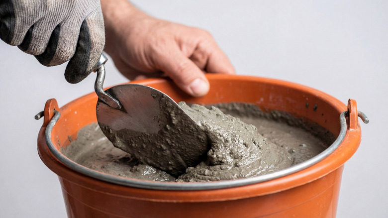 Person mixing concrete in a bucket with a trowel
