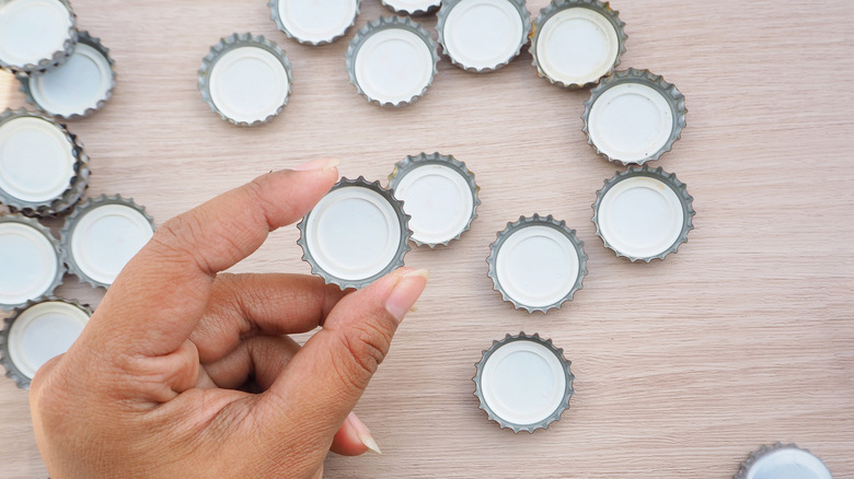 Bottle caps on a counter with a hand holding one