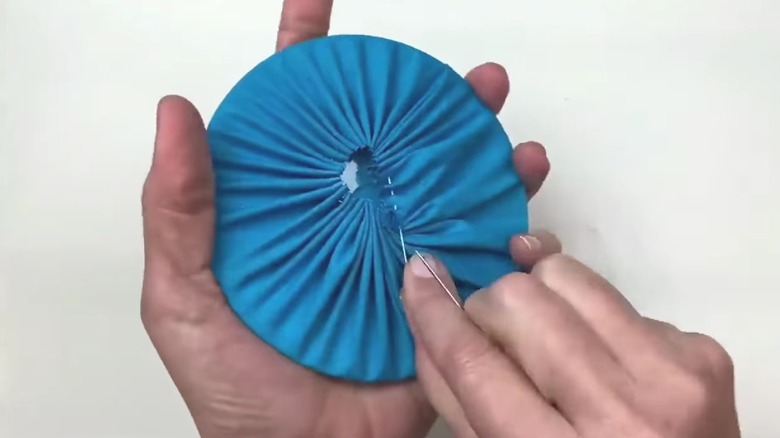 Hands sewing blue fabric around a CD.
