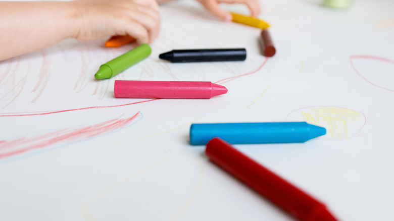 Child's hands drawing with crayons on white paper
