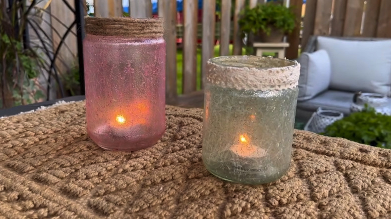 Two crayon crackle candle holders on a table with a brown cloth mat and a patio in the background