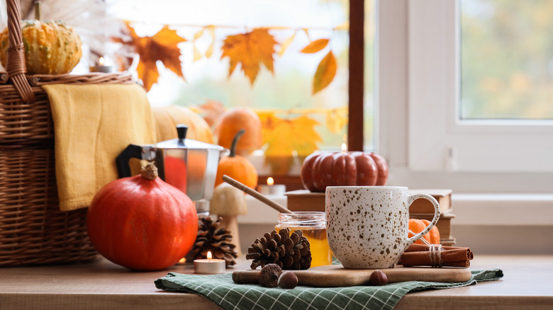Fall table display with a wicker basket, pumpkins, pine cones, honey, and a cup of coffee