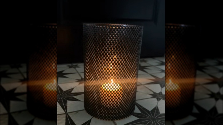 A candle burning within a hurricane vase covered in shelf liner