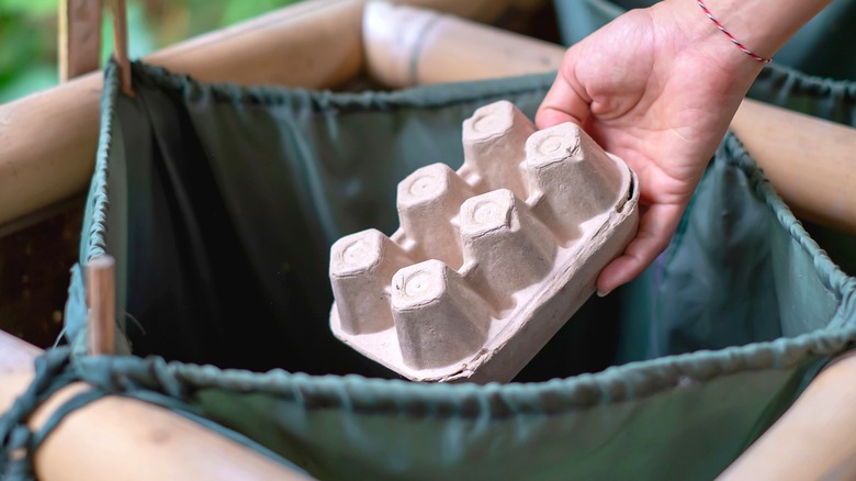 A person placing an empty egg carton into a recycling bin