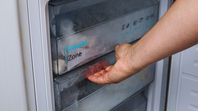A hand grabs the handle of a freezer shelf while starting to pull it out.