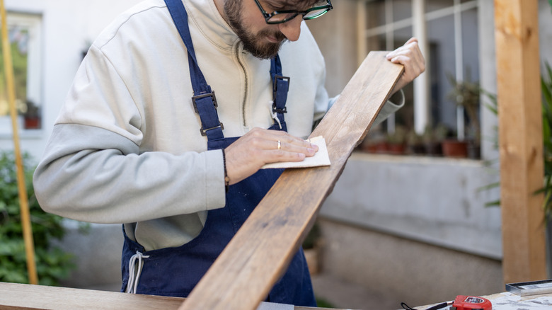 A person sands an aged wooden plank outdoors