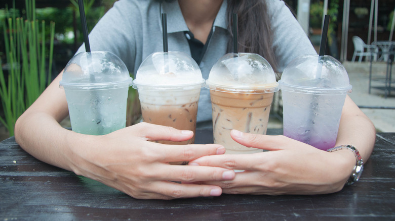 A woman is hugging four drink cups in her arms