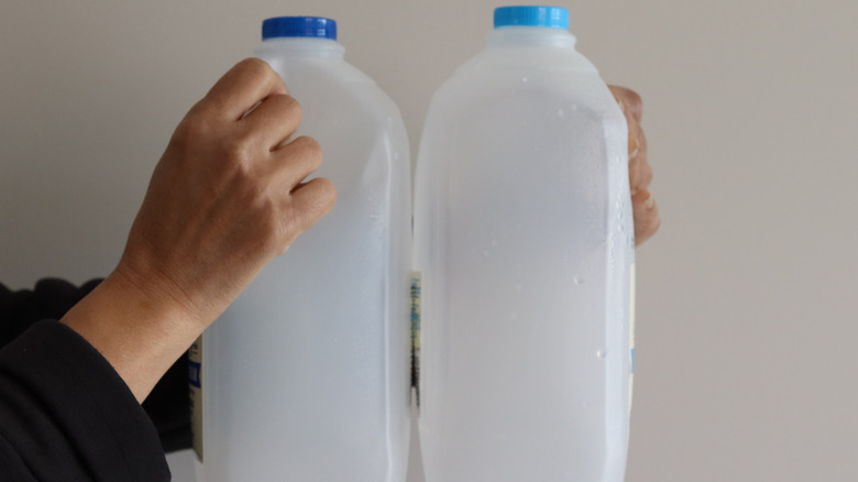 Person holding two empty milk jugs