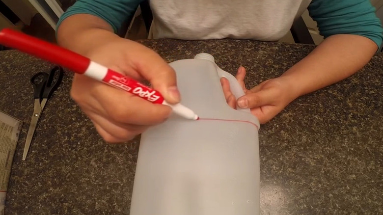 person drawing line on empty milk bottle with marker