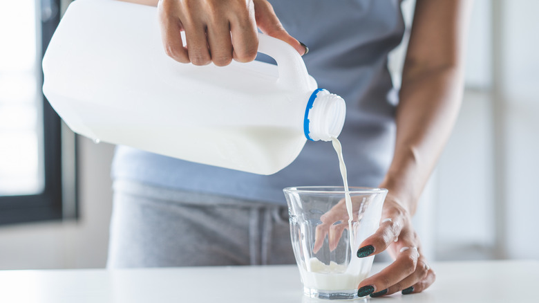 A person pouring milk into a glass from a plastic milk jug with a handle