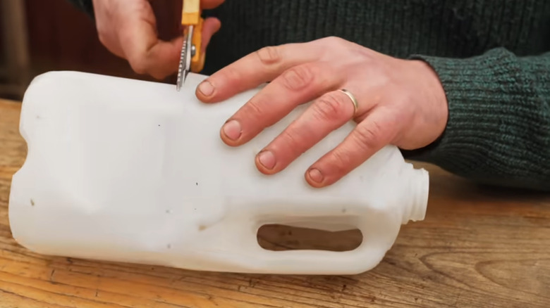Someone using scissors to cut a milk jug