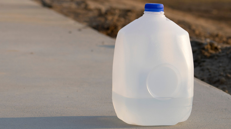 A jug 1/4 full of water stands on a sidewalk.