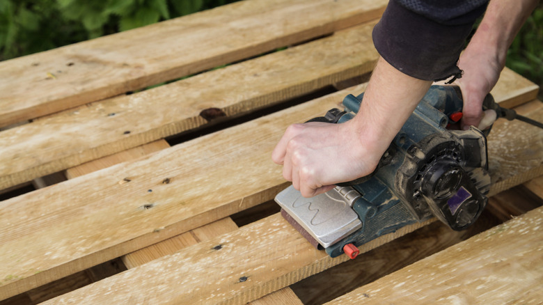 Person operating an electric sander on a wood pallet