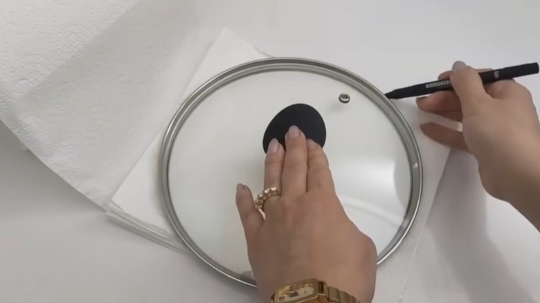 person tracing a pot lid with a pen on paper towel sheets