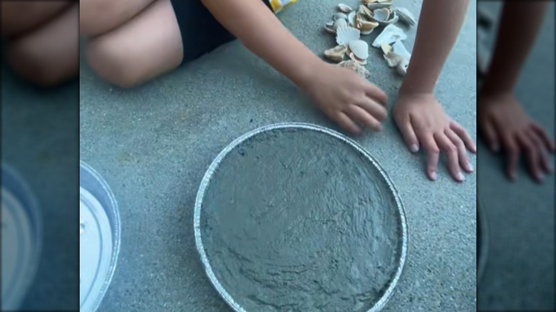 A child begins making a paving stone that will be filled with seashells.