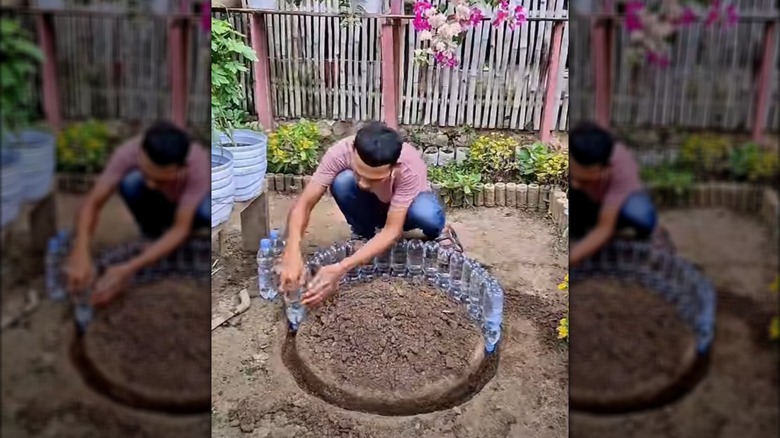 Person building a raised garden bed using plastic water bottles